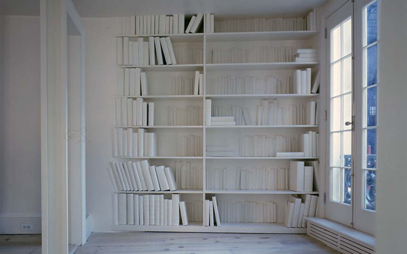 A wall full of books that have been murdered with white paint